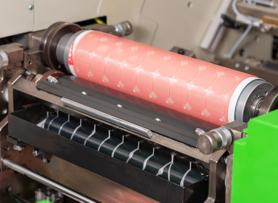 Industrial coating machine with a pink patterned roller applying finish to packaging material
