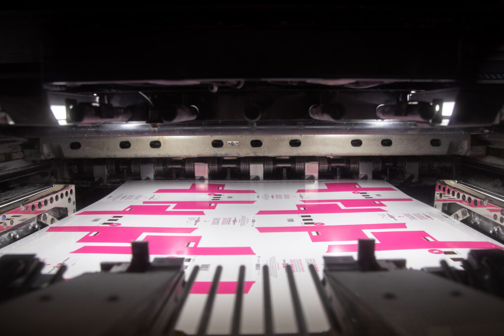 Printed pink and white packaging sheets moving through a converting and finishing press